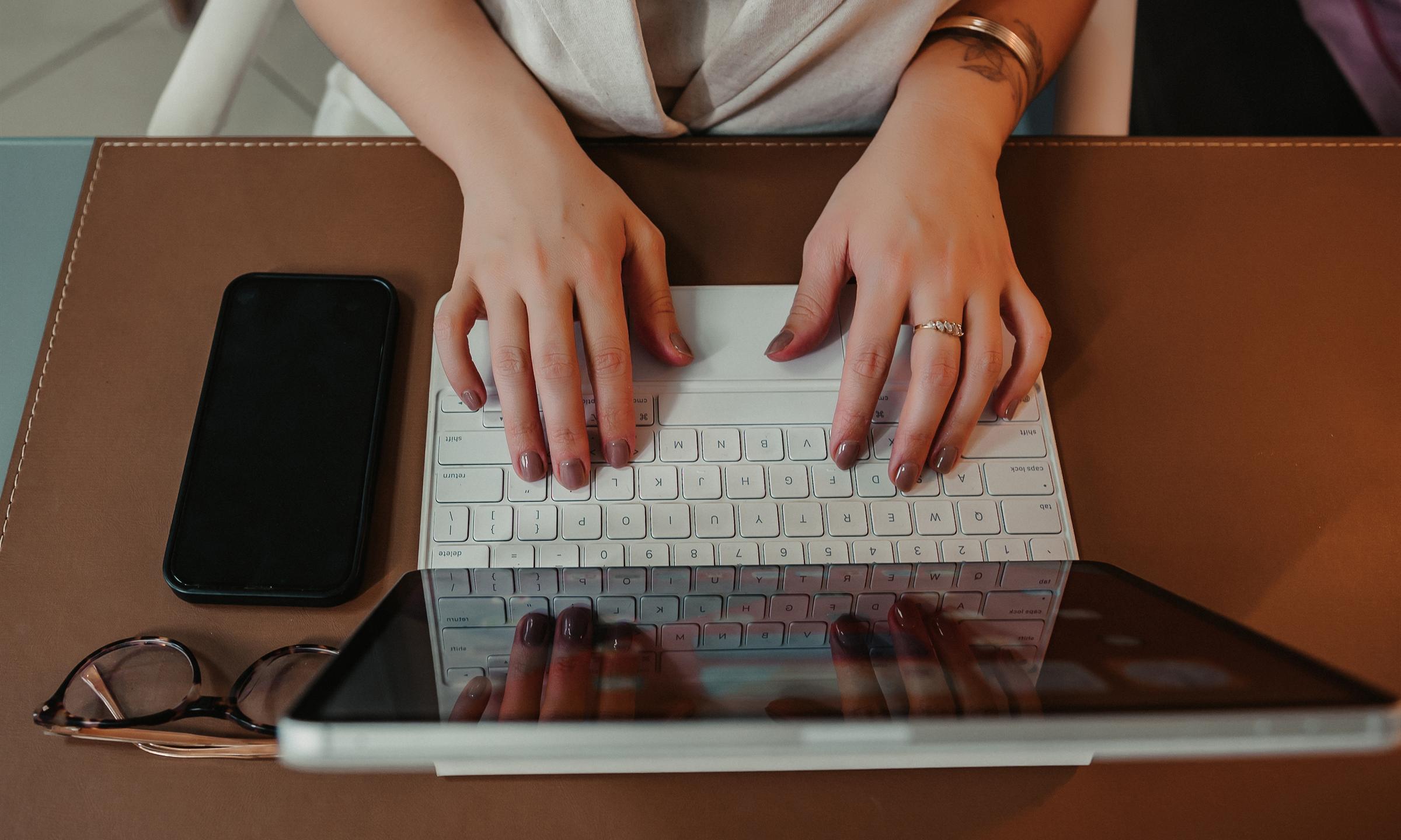 Mani sulla tastiera, tablet e telefono sulla scrivania